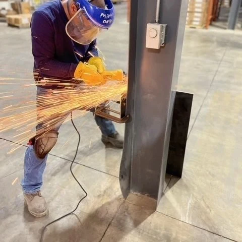 A Capital M welder grinding a fabricated structural steel column in the shop